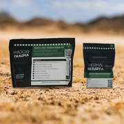 TRAUMA RESPONSE FEILD PACK.  Two product pouches for wound care are displayed on sandy desert ground with a blurred outdoor background. The larger pouch on the left is labeled 'MAJOR TRAUMA' and the smaller pouch on the right is labeled 'THERMAL INJURY'.